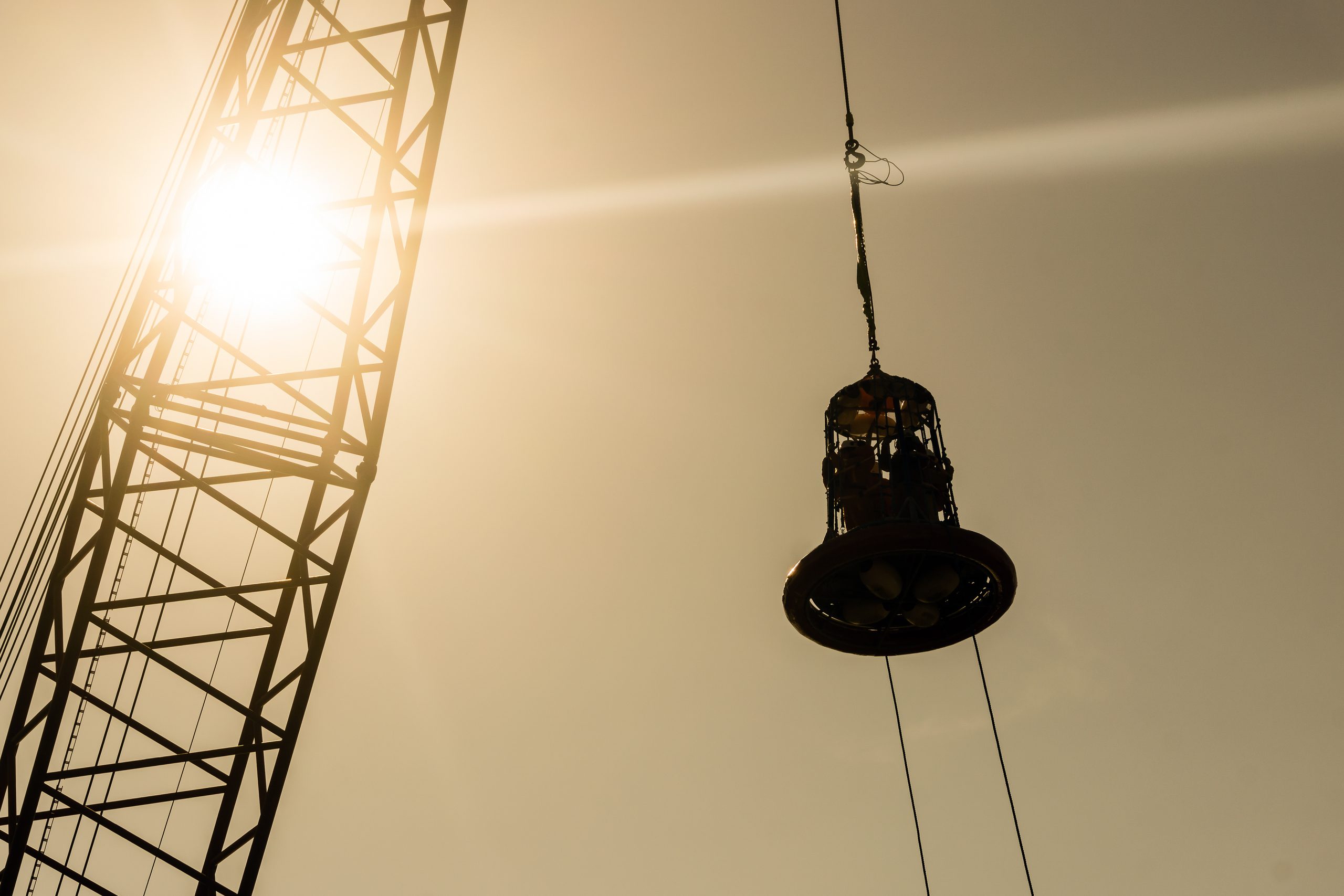 Silhouette of personal transfer basket being lifteed by a crane at oil field