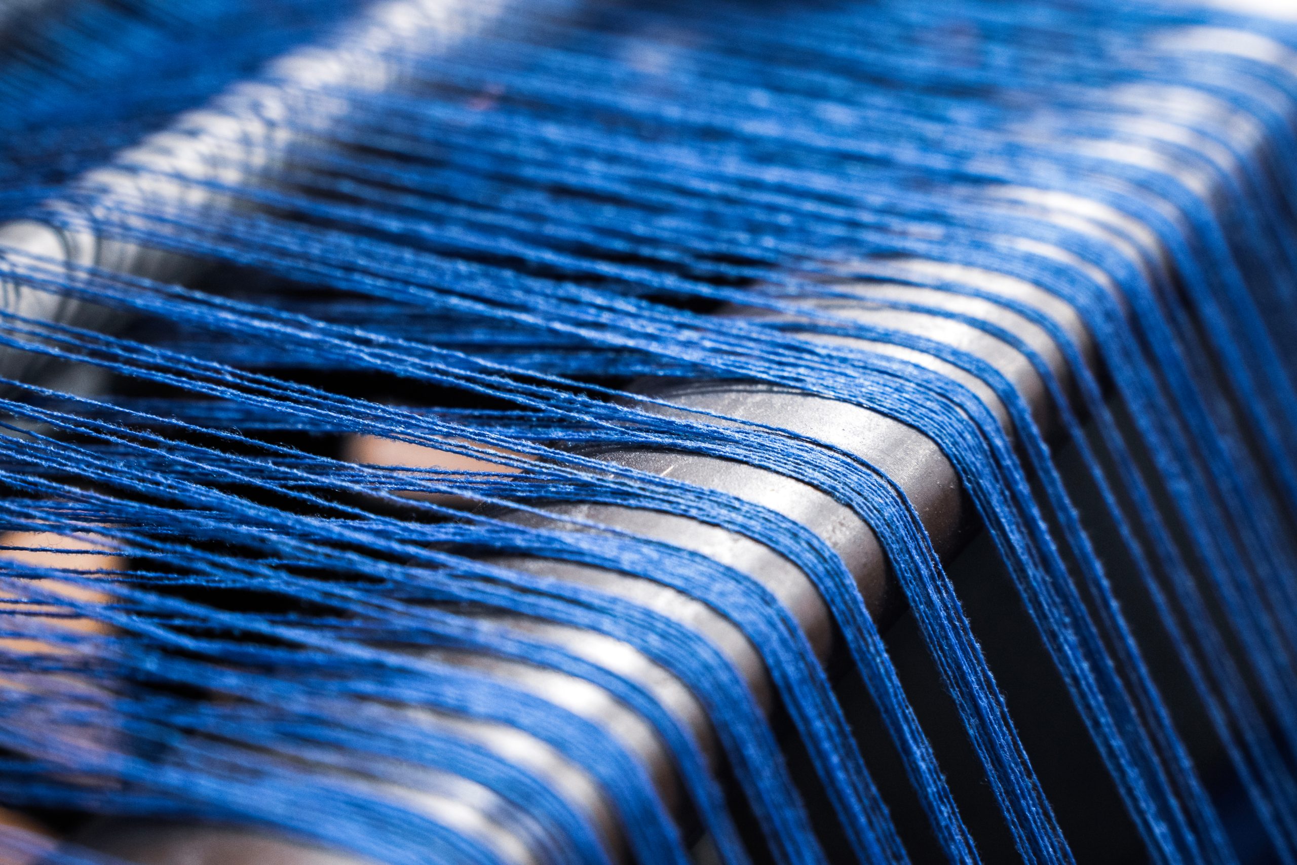A close up of weaving machine. A loom machine for clothing or woven label. Weaving machine for garment industry. Yarn thread lines on the weaving loom machine for clothing  in textile factory.
